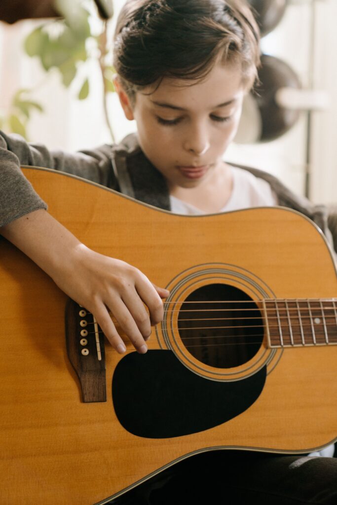 pexels-photo-4708904-4708904 A child engages in music, strumming an acoustic guitar with focus and passion.